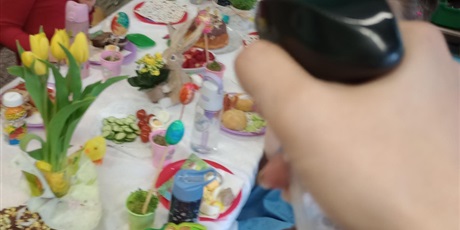 Powiększ grafikę: Śmigus dyngus. Dzieci siedzą przy stole i są opryskane wodą. Na ich twarzach widać zaskoczenie i radość.