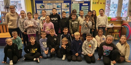 Powiększ grafikę: Grupa dzieci wraz z nauczycielką pozuje do zdjęcia. Za nimi znajdują się granatowe tablice z prezentacją pt. W 8 DNI DOOKOŁA ŚWIATA.