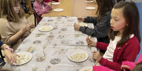 Powiększ grafikę: Grupa dzieci siedzi przy stole. Przed nimi stoją talerzyki z popcornem, który dzieci jedzą drewnianymi pałeczkami.