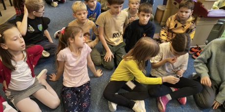 Powiększ grafikę: Grupa dzieci siedzi na dywanie. Dwie dziewczynki trzymają słoiczki z przyprawami pochodzącymi z Azji.