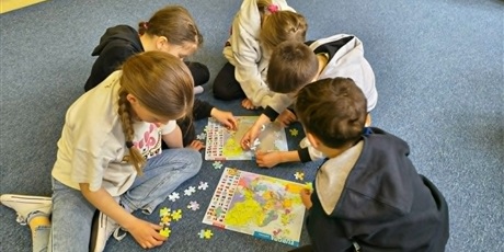 Powiększ grafikę: Grupa dzieci siedzi na dywanie i wspólnie układa puzzle przedstawiające mapę Europy.