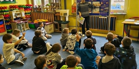 Powiększ grafikę: Nauczycielka stoi przy granatowych tablicach i prezentuje wiadomości o Europie. Przed nią na dywanie siedzą uczniowie, którzy w skupieniu słuchają.