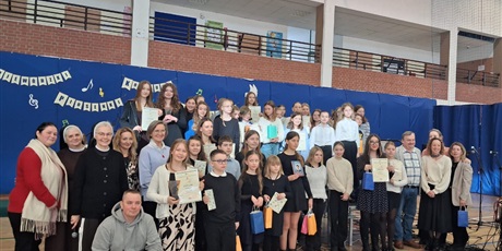 Powiększ grafikę: Uczestnicy i organizatorzy IV Wojewódzkiego Konkursu Piosenki Religijnej pozują do wspólnego zdjęcia z dyplomami i nagrodami w sali gimnastycznej.