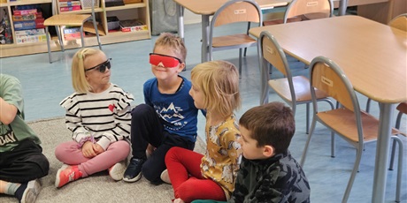 Powiększ grafikę: Na zdjęciu widaćchłopca, który ma założone czerwone okulary oraz dziewczynkę, która ma czarne okulary. Dzieci wcielają się w role osób z niepełnosprawnością wzroku.