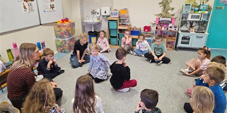 Powiększ grafikę: Grupa 6-letnich dzieci siedzi na dywanie w kole. Wewnątrz znajduje się dwoje dzieci.