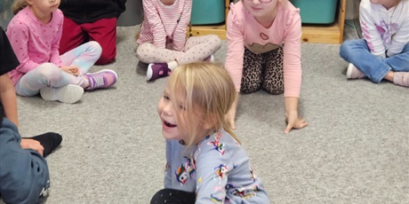 Powiększ grafikę: Dziewczynka siedzi na dywanie wewnątrz koła. Na ręku ma rękawicę bokserską. Śmieje się.