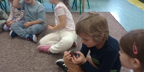 Powiększ grafikę: Dzieci siedzą na dywanie i oglądają bursztyn. Mają w rękach bryłki bursztynu.