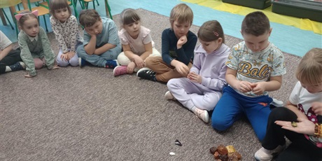 Powiększ grafikę: Dzieci siedzą na dywanie i oglądają bursztyn. Mają w rękach bryłki bursztynu.