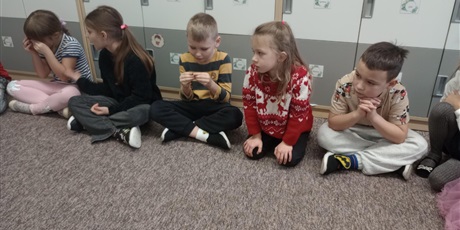 Powiększ grafikę: Dzieci siedzą na dywanie i oglądają bursztyn. Mają w rękach bryłki bursztynu.