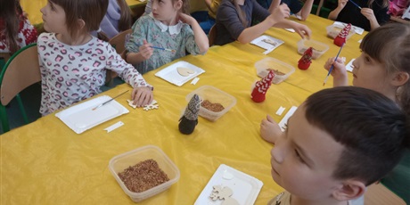 Powiększ grafikę: Grupa dzieci siedzi przy stoliku. Dzieci będą wykonywać doświadczenia związane z bursztynem.