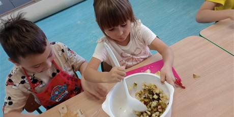 Powiększ grafikę: Dziewczynka miesza warzywa w misce. Chłopiec ma na sobie czerwony fartuszek kuchenny.