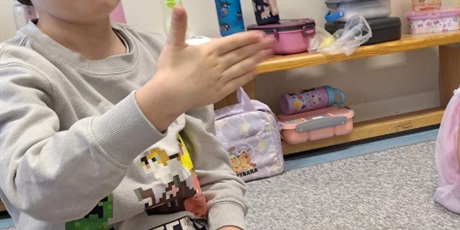 Powiększ grafikę: Chłopiec siedzi na dywanie i uczy się nowego słowa w języku migowym. Pokazuję ręką słowo - źle.