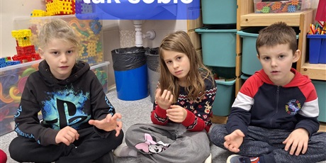 Powiększ grafikę: Troje dzieci siedzi na dywanie i pozkazuje rękowa kolejne słowo - tak sobie.