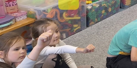 Powiększ grafikę: Dzieci mają wyciągnięte ręce i dłonie zwinięte w kulkę. Oznacza to kolejną literę - a.