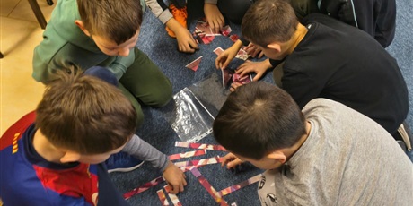 Powiększ grafikę: Grupa chłopców układa puzzle przedstawiające świąteczny obrazek.