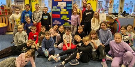 Powiększ grafikę: Grupa dzieci wraz z nauczycielką pozuje do zdjęcia. Z tyłu stoi granatowa tablica z kolorowymi napisami WESOŁYCH ŚWIĄT w różnych językach świata.