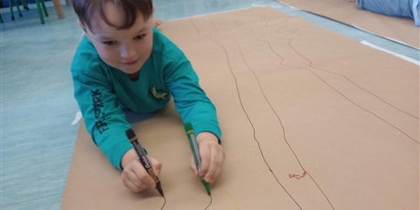 Powiększ grafikę: Chłopiec maluje obraz na szarym papierze mazakami. Jest bardzo szczęśliwy i uśmiechnięty.