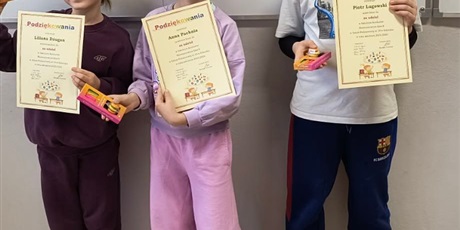 Powiększ grafikę: Uczniowie stoją obok siebie, w tle tablica. Prezentują dyplomy.