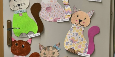 Powiększ grafikę: Szare drzwi z pracami plastycznymi przedstawiającymi kolorowe koty.