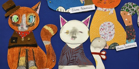 Powiększ grafikę: Granatowa tablica ścienna z pracami plastycznymi przedstawiającymi kolorowe koty.