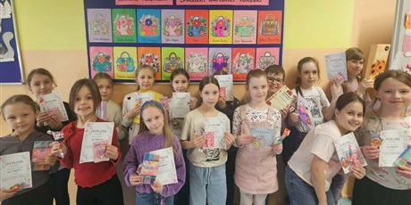 Powiększ grafikę: Grupa dzieci pozuje do zdjęcia na tle granatowej tablicy z kolorowymi pracami konkursowymi pt. "Projekt damskiej torebki". W rękach trzymają dyplomy i nagrody.