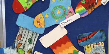 Powiększ grafikę: Granatowa tablica, na której wiszą prace plastyczne, które przedstawiają kolorowe skarpety z motywami świątecznymi, zimowymi. 