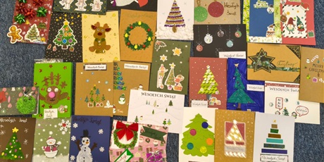 Powiększ grafikę: Kolorowe kartki bożonarodzeniowe leżą ułożone na podłodze. Są na nich namalowane lub wyklejone bałwanki, choinki, bombki itp.