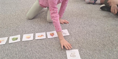 Powiększ grafikę: Dziewczynka siedząc na dywanie dopasowuje obrazek do zapisanego wyrazu. Na twarzy widać skupienie oraz radość i satysfakcje z wykonanego zadania.