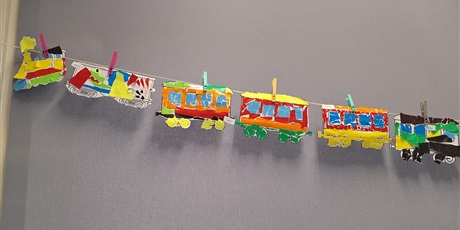 Powiększ grafikę: Fragment dekoracji: Do sznurka przyczepiono spinaczami lokomotywę z wagonikami. Są one zrobione z papieru i pomalowane farbkami.