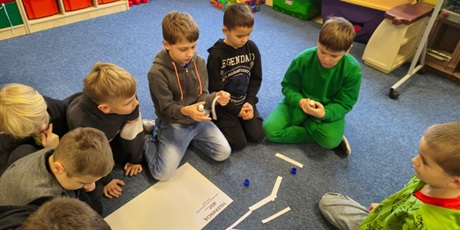 Powiększ grafikę: Grupa chłopców siedzi na dywanie w świetlicy. Pochylają się nad plakatem, na który przyklejają karteczki z przykładami tolerancji.