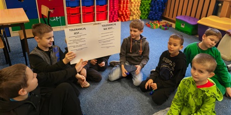 Powiększ grafikę: Grupa chłopców siedzi na dywanie w świetlicy. Dwóch chłopców trzyma w rękach plakat uniesiony do góry, który wspólnie wykonali.