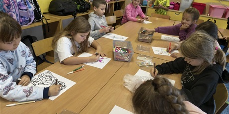 Powiększ grafikę: Grupa dzieci siedzi przy stole w świetlicy. Uczniowie kolorują mazakami obrazki ze zwierzętam w ramach konkursu "Zwierzęta w geometrii". 