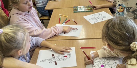 Powiększ grafikę: Grupa dzieci siedzi przy stole w świetlicy. Uczniowie kolorują mazakami obrazki ze zwierzętam w ramach konkursu "Zwierzęta w geometrii". 