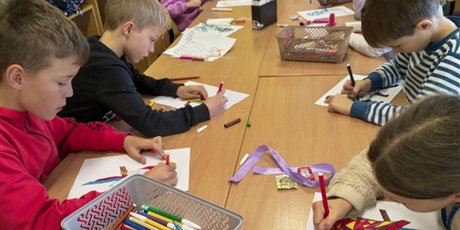 Powiększ grafikę: Grupa dzieci siedzi przy stole w świetlicy. Uczniowie kolorują mazakami obrazki ze zwierzętam w ramach konkursu "Zwierzęta w geometrii". 