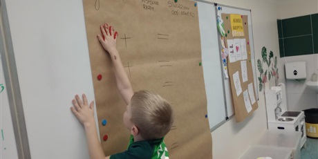 Powiększ grafikę: Uczniowie oddziału przedszkolnego odciskają dłonie zanurzone w farbie na papierze.