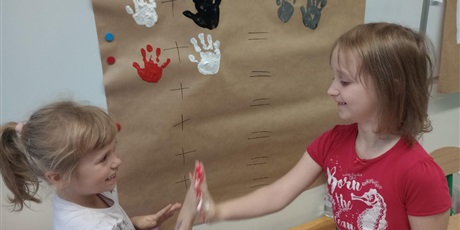 Powiększ grafikę: Uczniowie oddziału przedszkolnego przyciskają do siebie dłonie zanurzone w farbie.