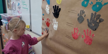 Powiększ grafikę: Uczniowie oddziału przedszkolnego odciskają dłonie zanurzone w farbie na papierze.