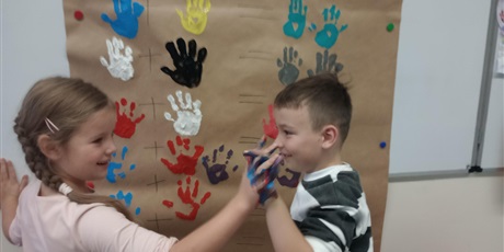 Powiększ grafikę: Uczniowie oddziału przedszkolnego przyciskają do siebie dłonie zanurzone w farbie.