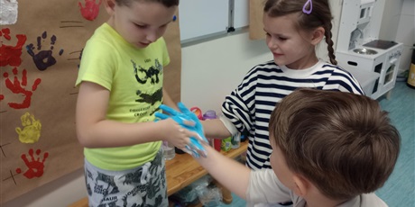 Powiększ grafikę: Uczniowie oddziału przedszkolnego przyciskają do siebie dłonie zanurzone w farbie.