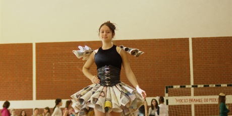 Powiększ grafikę: Zdjęcie przedstawia uczennicę prezentującą zrobiony przez nią strój na pokazie pod tytułem „Moda Ekologiczna”. Spódniczka i rękawy wykonane są z gazet.