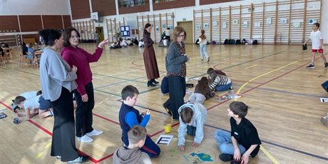 Powiększ grafikę: Zdjęcie przedstawia uczniów, którzy w swoich grupach robią plakaty związane z obchodami Dnia Ziemi. Wokół nich chodzą nauczycielki, oceniające prace konkursowe i przyznające punkty każdej z nich.