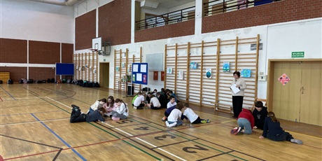 Powiększ grafikę: Zdjęcie ukazuje uczniów w grupach układających puzzle. Po prawej stronie stoi nauczycielka obserwująca ich zaangażowanie