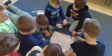 Powiększ grafikę: Grupa chłopców siedzi na dywanie w kole i przykleja hasła na "Słowniczek Zazdrości".