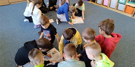 Powiększ grafikę: Dwie grupy dzieci siedzące na dywanie w świetlicy. Dzieci naklejają hasła na "Słowniczek Zazdrości"