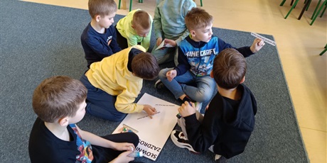 Powiększ grafikę: Grupa chłopców przykleja hasła na "Słowniczek Zazdrości".