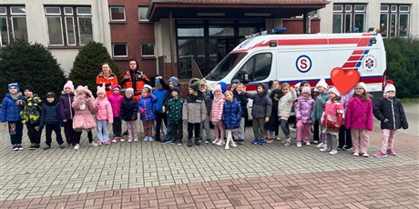 Powiększ grafikę: Dzieci stoją przed szkołą. W tle wyraźnie widać pracowników pogotowia oraz karetkę.