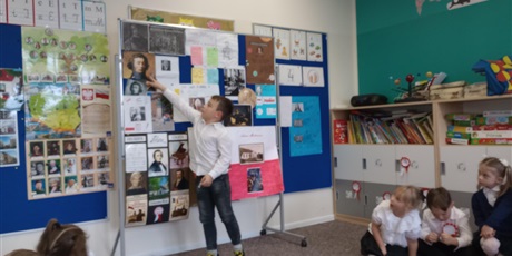 Powiększ grafikę: Chłopiec pokazuje na obraz znanego Polaka. Opowiada o nim koleżankom i kolegom.