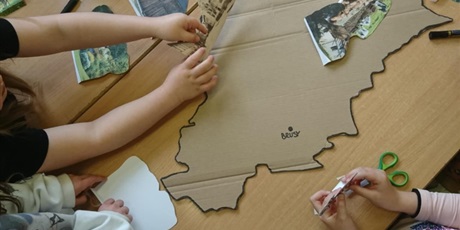Powiększ grafikę: Na stole leży kontur mapy Kaszub oraz zdjęcia tego regiony. Dzieci układają makietę ze zdjęć.