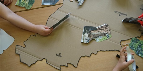 Powiększ grafikę: Na stole leży kontur mapy Kaszub oraz zdjęcia tego regiony. Dzieci układają makietę ze zdjęć.