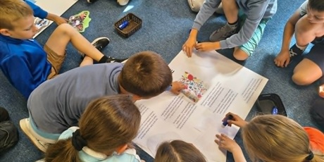 Powiększ grafikę: Grupa dzieci pochyla się nad białym brystolem i przykleja ilustracje związane z Kociewiem.